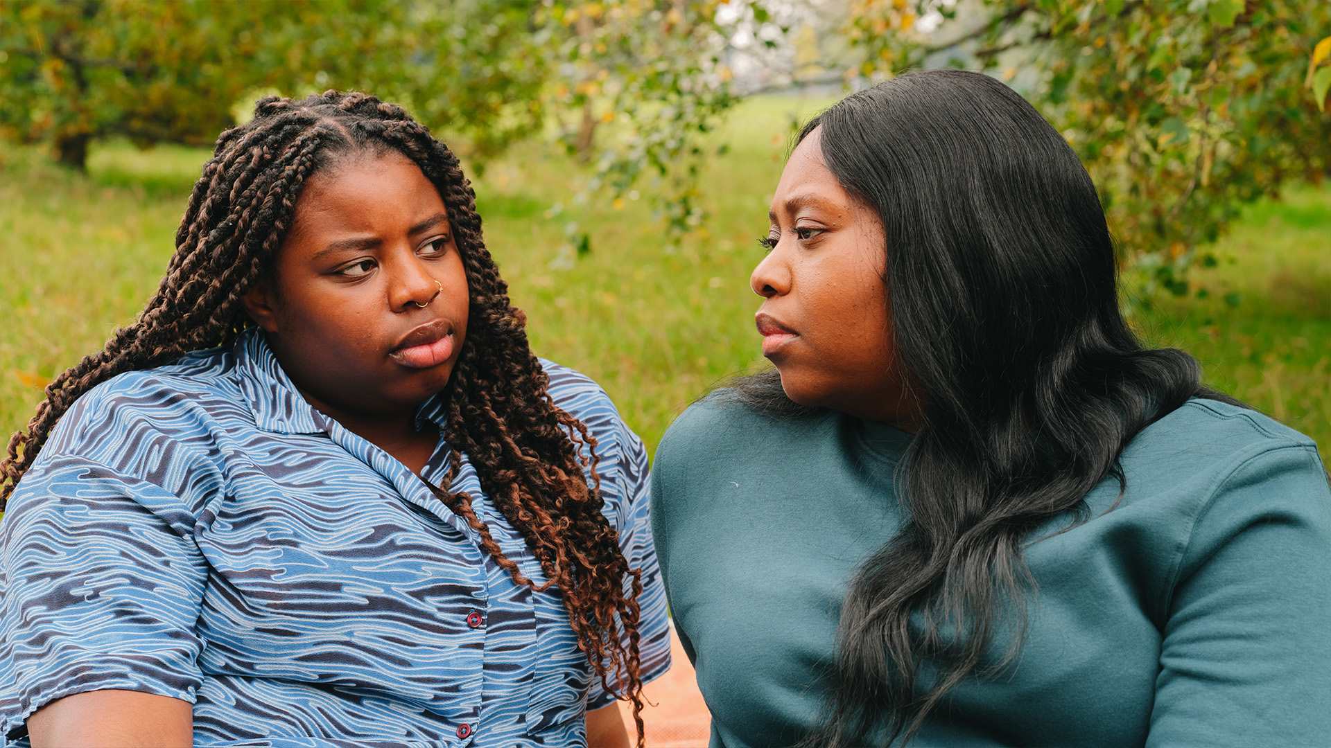 A young Black woman talking about something serious with an older Black woman in the park.