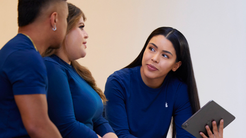 Tres empleados de Apple Retail hablando, una de ellas sostiene un iPad.