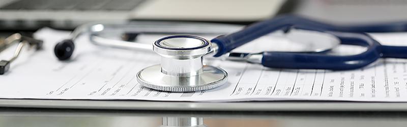 Stethoscope head lying on medical form on clipboard pad 