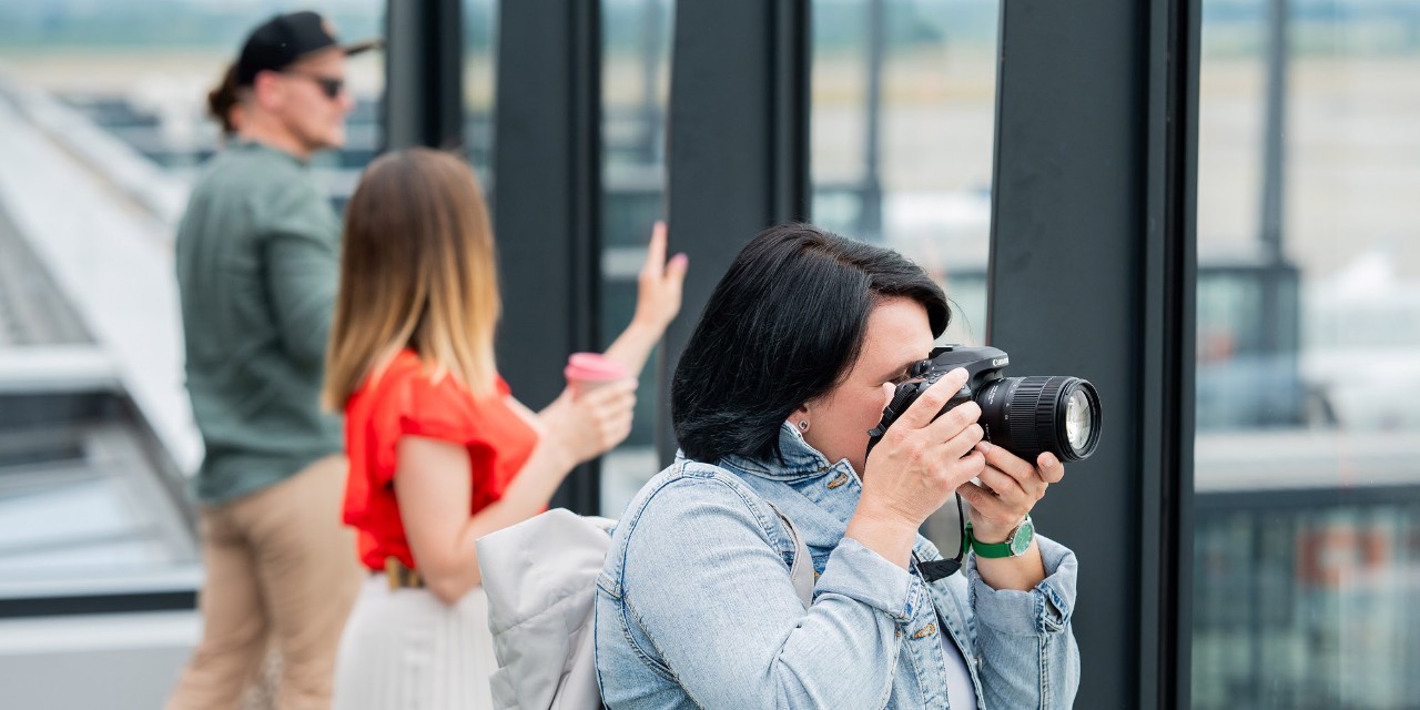 3 people on the visitors terrace. 1 Person has a camera in front of the head