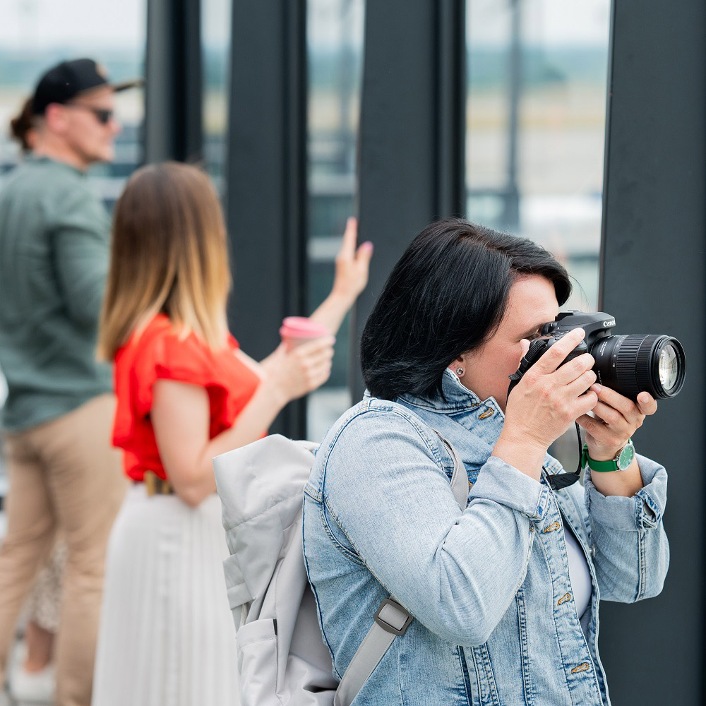 3 people on the visitors terrace. 1 Person has a camera in front of the head