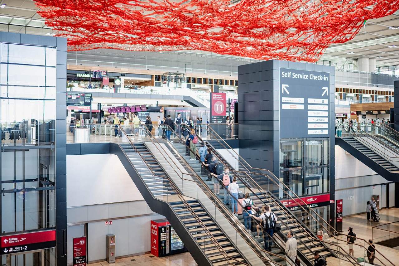 View of the Terminal 1 check-in hall, including the artwork "The Magic Carpet". The picture also shows the travelling chairs and check-in counters.