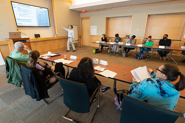 group of adults sitting in conference room looking at person presenting information on large screen