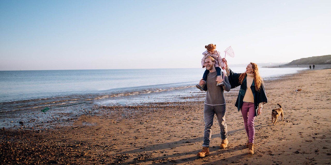 Family with a dog walk along a beach