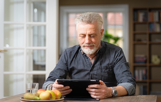 gråhåret mand sidder med tablet ved spisebord