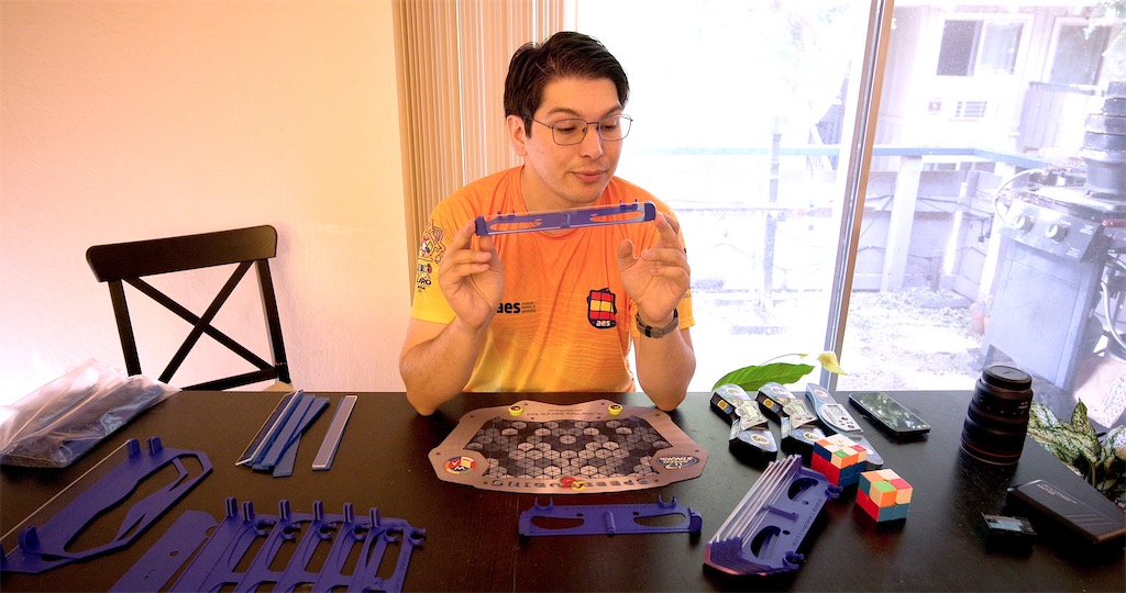 Video frame of Lucas Garron holding up a prototype, surrounded by several iterations of prototypes on a table.