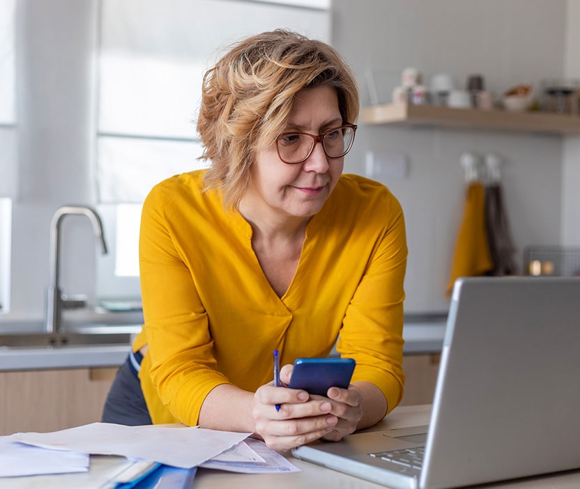 Photo of a woman considering a credit lock vs. freeze as she looks at her phone and computer.