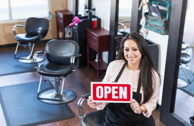 Salon grand opening ideas - stylist holding an open sign in a salon.