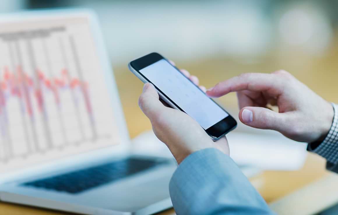 Hands shown typing on phone with laptop in background