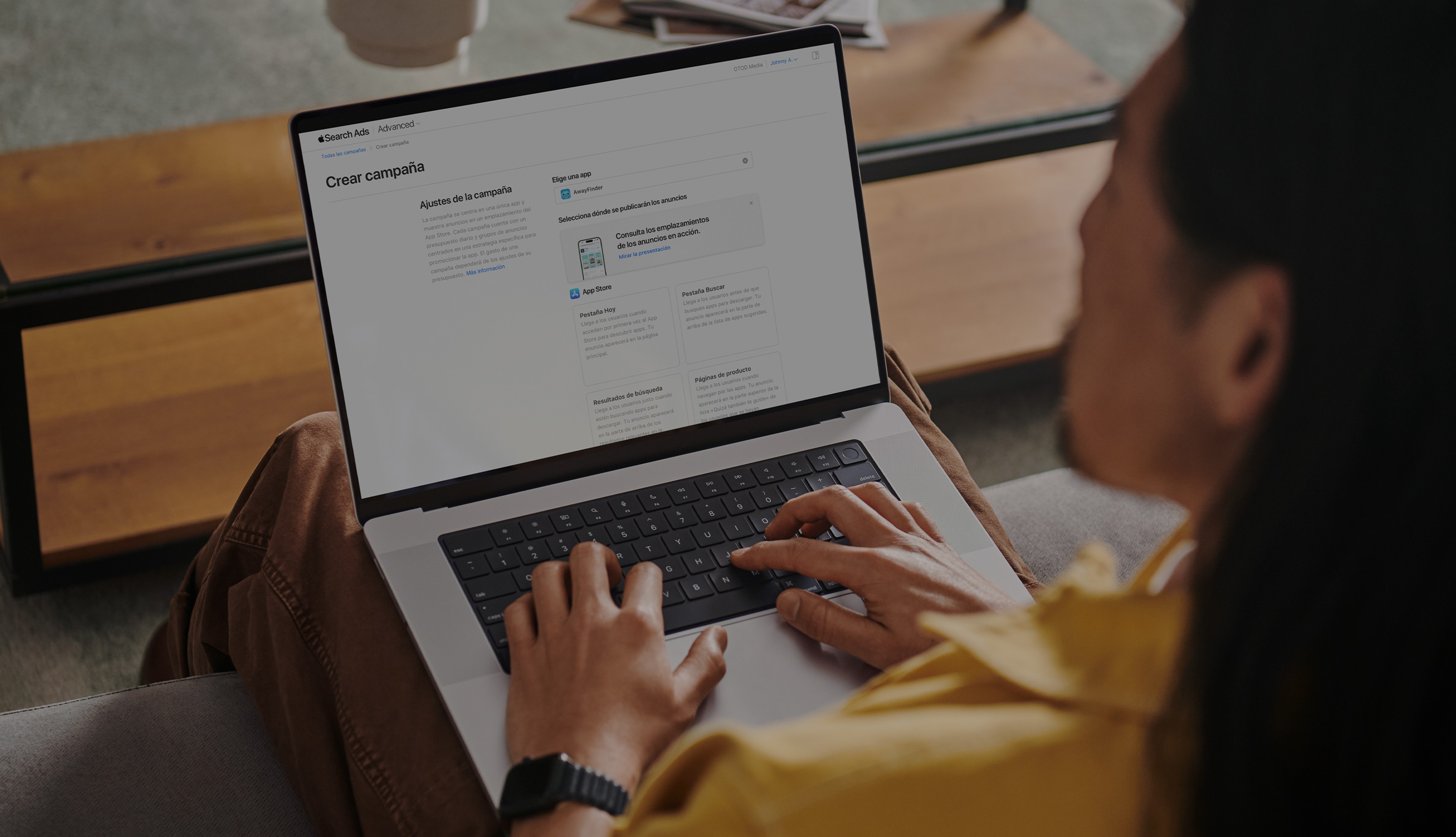 Un anunciante trabajando en un MacBook. La página «Crear campaña» de Apple Search Ads está abierta en la pantalla y muestra cuatro ubicaciones de anuncios disponibles: pestaña Hoy, pestaña Buscar, resultados de búsqueda y páginas de producto.