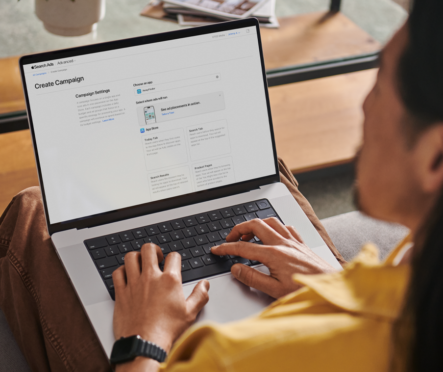 A person working on a MacBook creates a new campaign in Apple Search Ads.