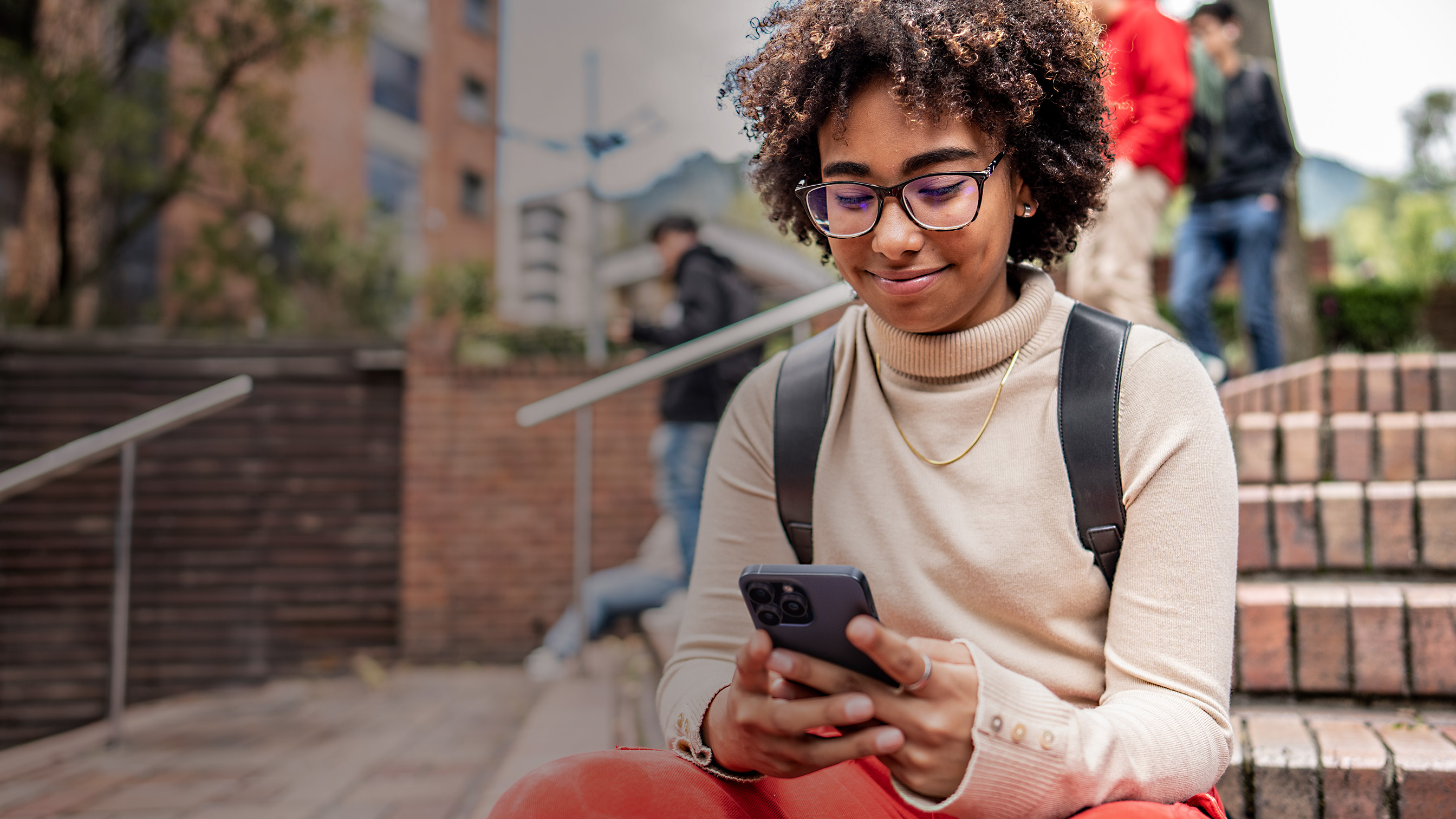 Una persona seduta all’esterno sorride mentre guarda il proprio iPhone.