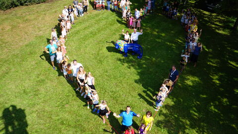 Gruppenbild von Eltern mit Kindern vom Drillingstreffen 2021. Auf dem Foto stehen die Eltern mit Kindern auf einer sonnenbeschienenen Wiese und haben sich so angeordnet, dass es aussieht wie ein Herz.