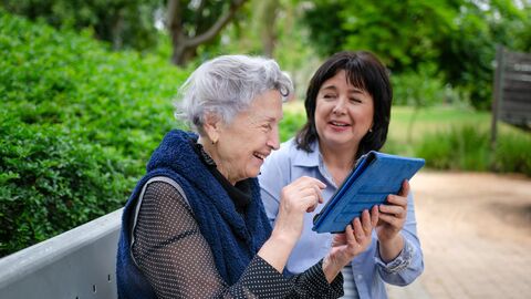 Zwei Frauen sitzen mit einem Tablet-PC auf einer Bank 