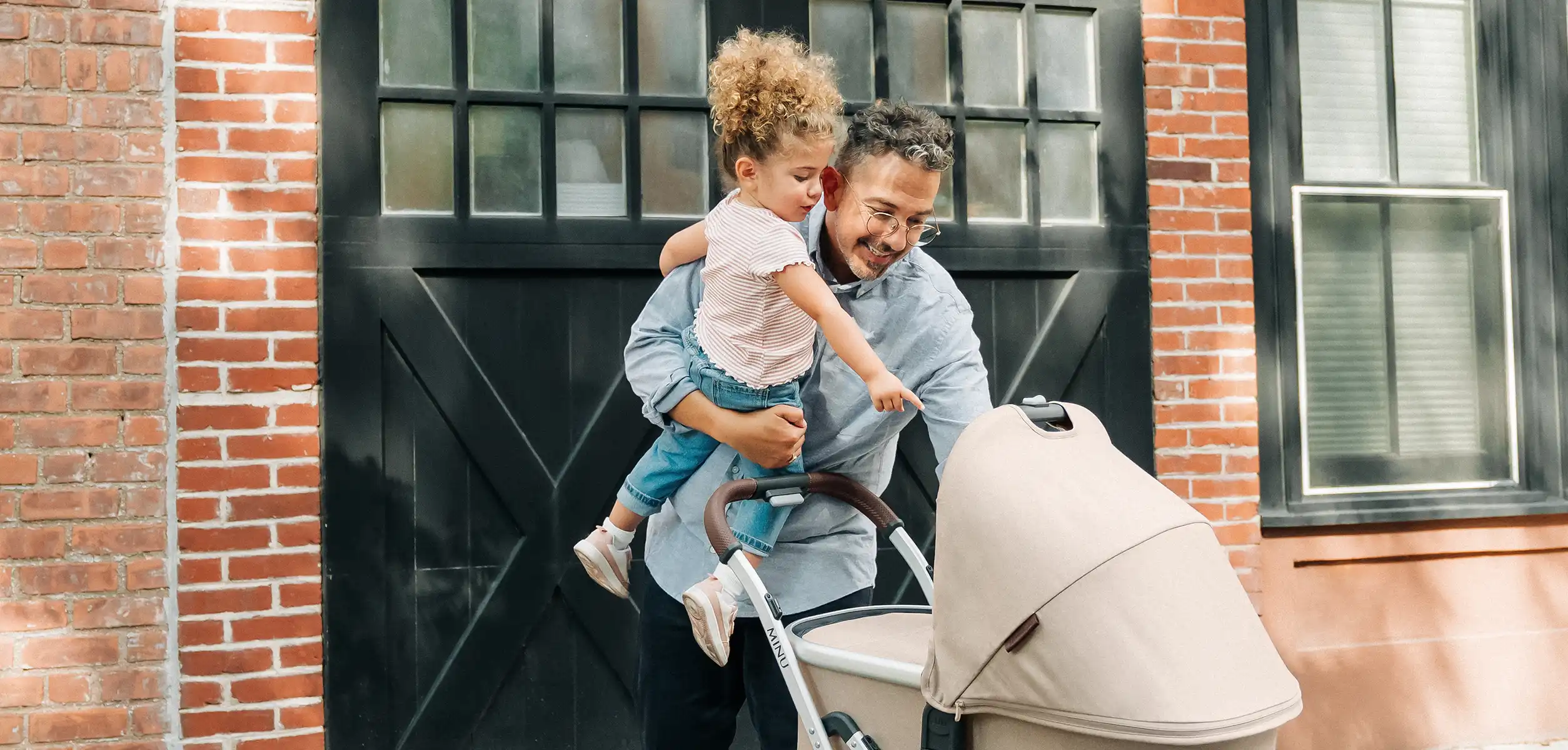 A father and toddler daughter look over a newborn addition to the family in the Bassinet attachement, which attaches to the Minu V2 frame with the help of convinient adapters