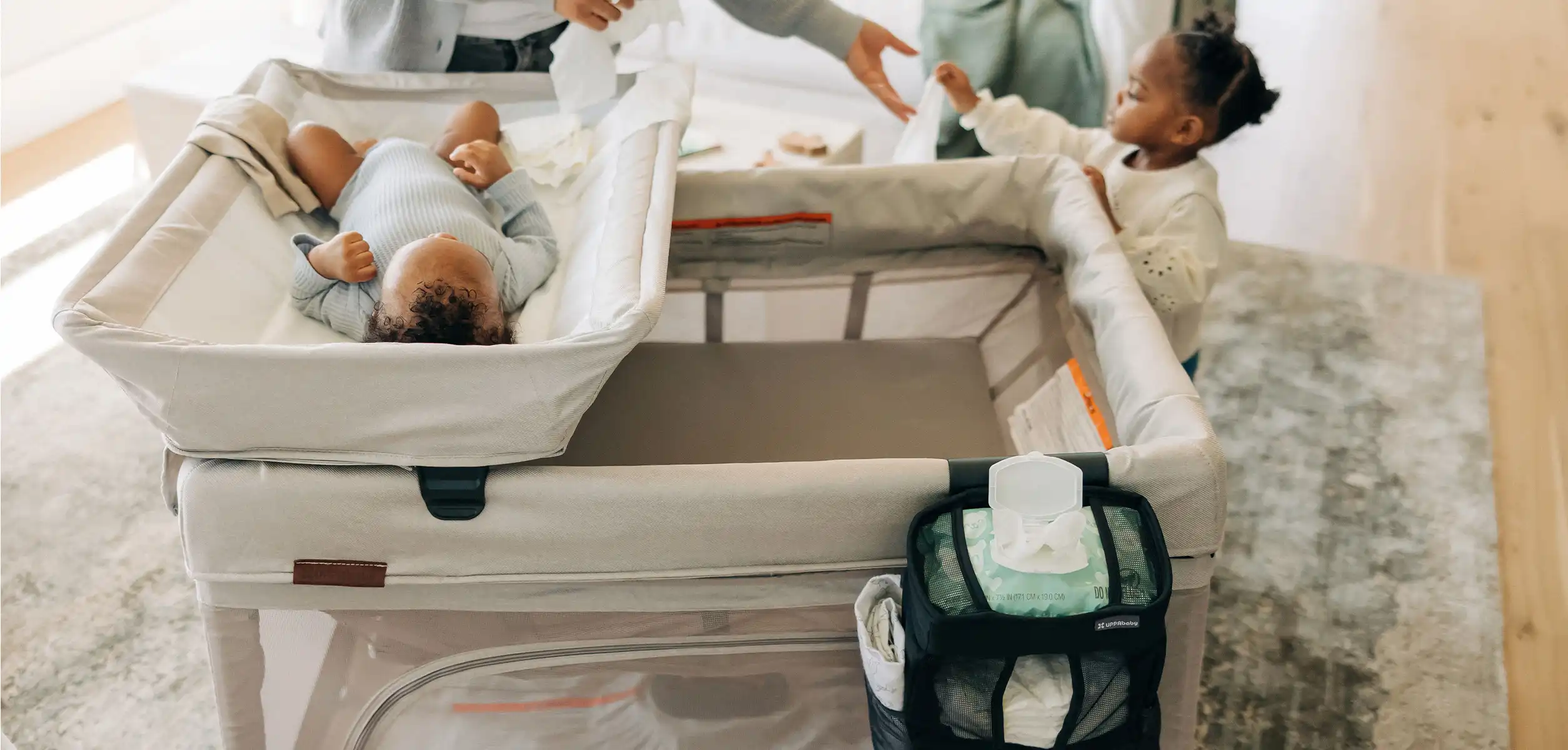 An infant lays in the Remi Changing Station accessory for easy access for a quick change; all the items the woman needs are convenietly nearby in the Changing Station Organizer