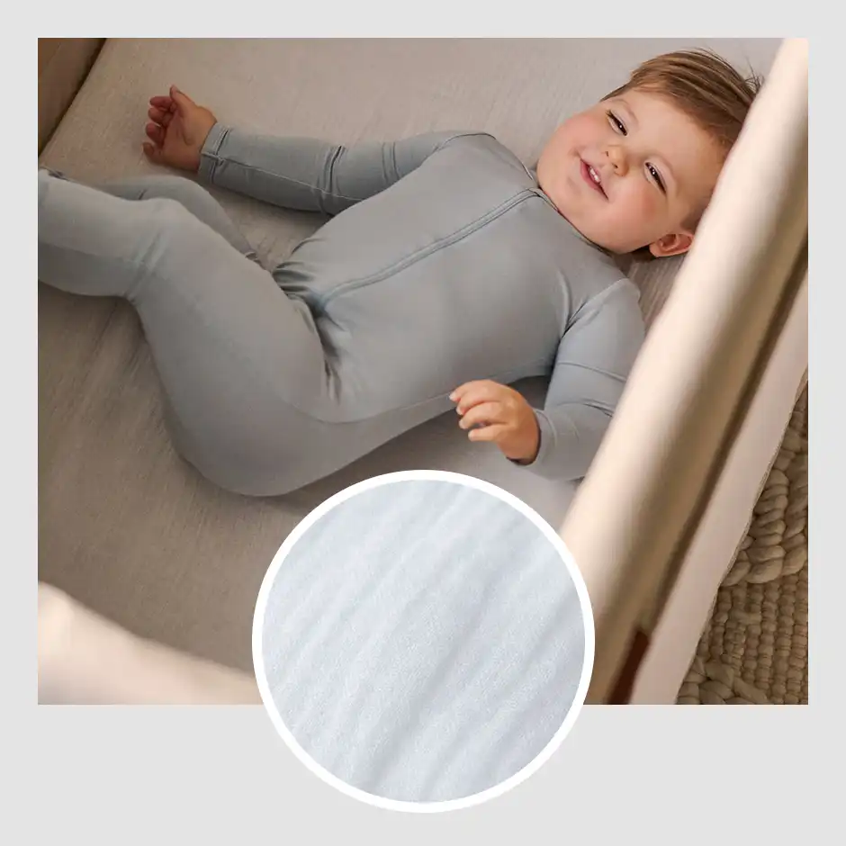 A smiling child comfortably lays on the Remi's included mattress cover that provides additional softness and breathability