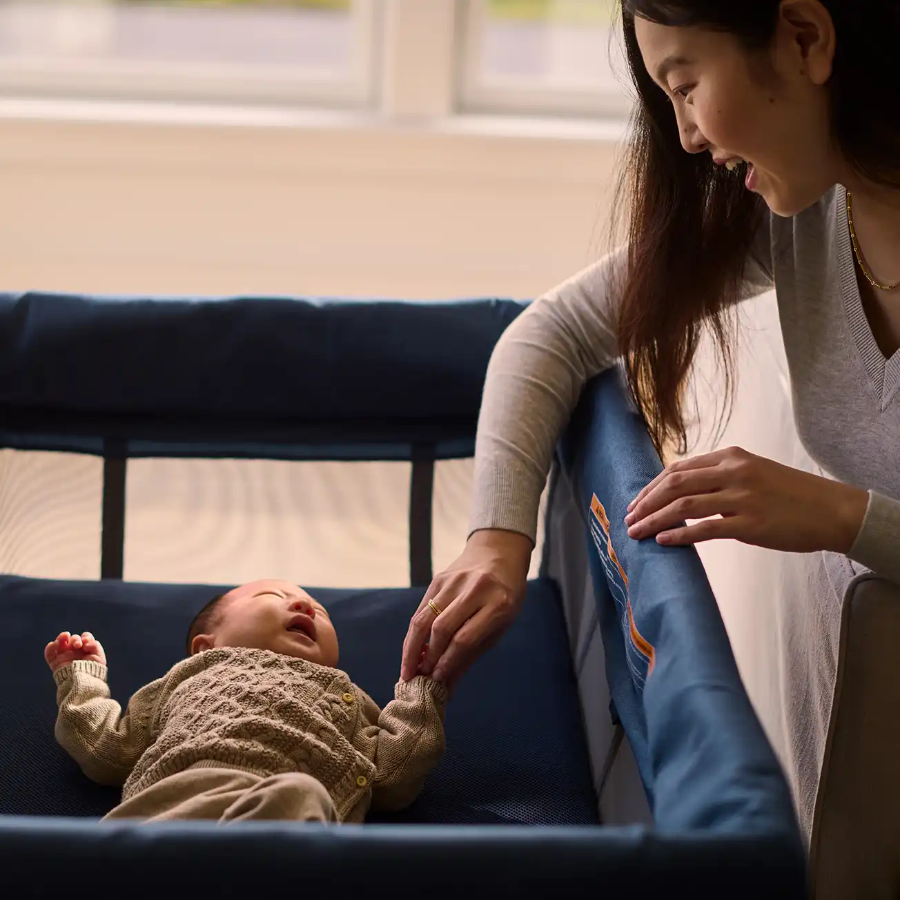 A woman tends to her child laying the Remi's included Bassinet that transforms the Remi from a play space to a ventilated newborn bedside solution