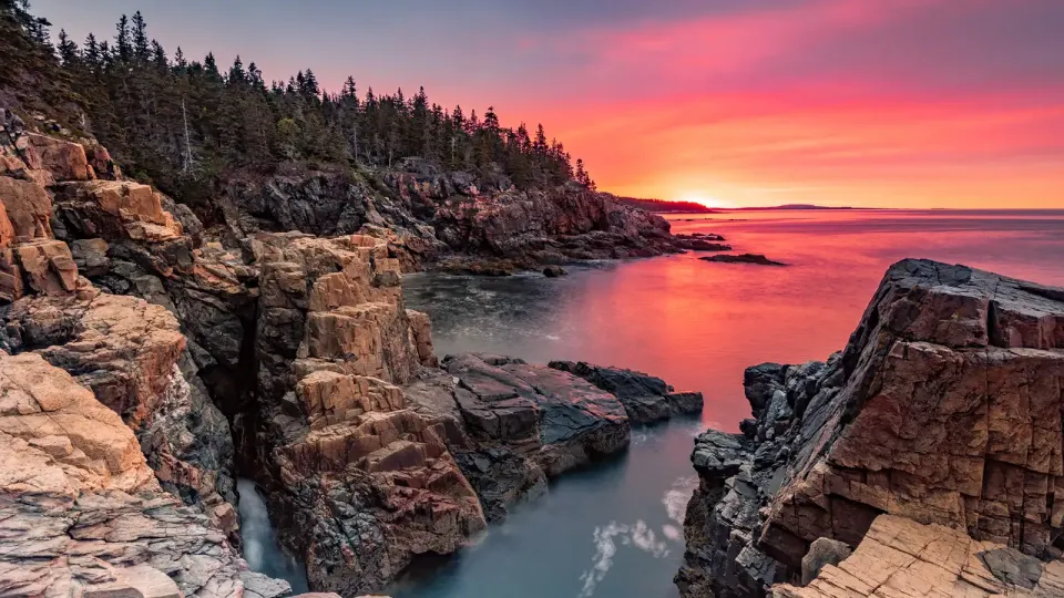 Rocky coast of Maine with pink and orange sunset over the water