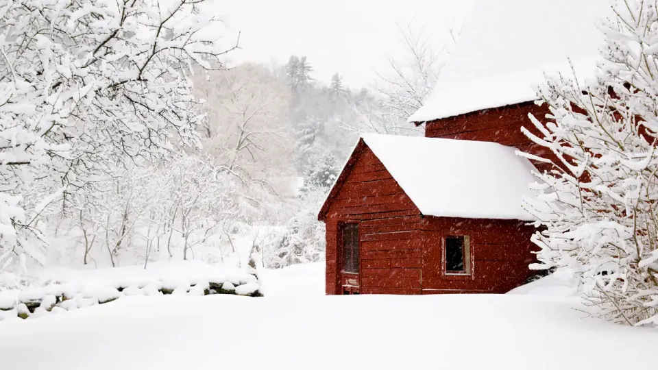 Heavy snow drapes trees and surrounds old, red farmhouse