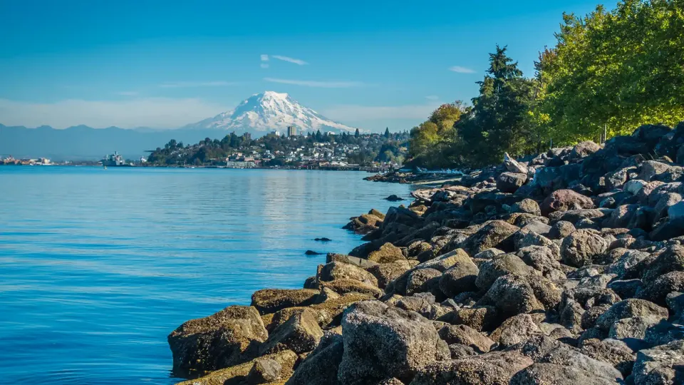 Snow capped Mount Rainier and the port city of Tacoma in the distance from a rocky shoreline