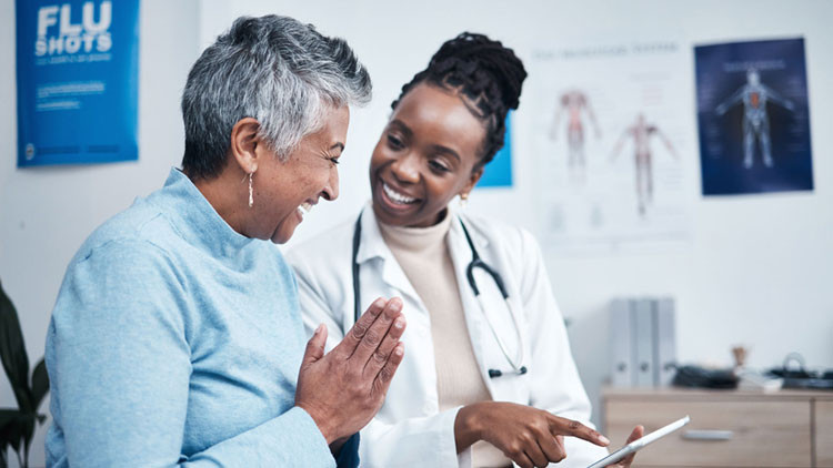 A doctor reviews test results with her patient. She points at her tablet and they are both smiling.