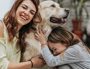 Eine glückliche Familie, bestehend aus einer Frau, einem Kind und einem großen Hund, die gemeinsam lachen und kuscheln.