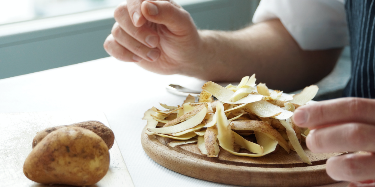 Eine Person sitzt vor einem Holzbrett mit Kartoffelschalen