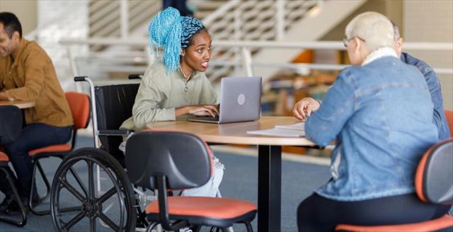 Student in wheelchair sits at table talking with other students