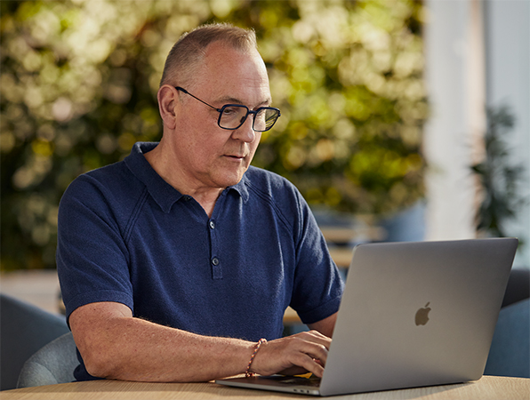 Applen ohjelmisto‑ ja palvelutiimin työntekijä tekee töitä ulkona MacBookilla, taustalla näkyy viherkasveja.