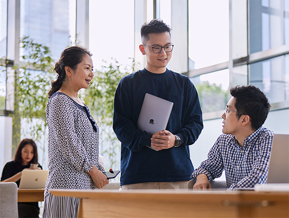 床から天井までが窓になっている部屋で、3人のオペレーション＆サプライチェーン職のApple社員が話している。