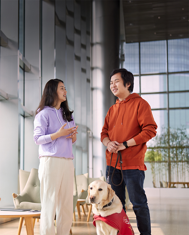 Deux membres du personnel d’Apple discutent dans un espace commun lumineux. L’un tient en laisse un chien d’assistance.