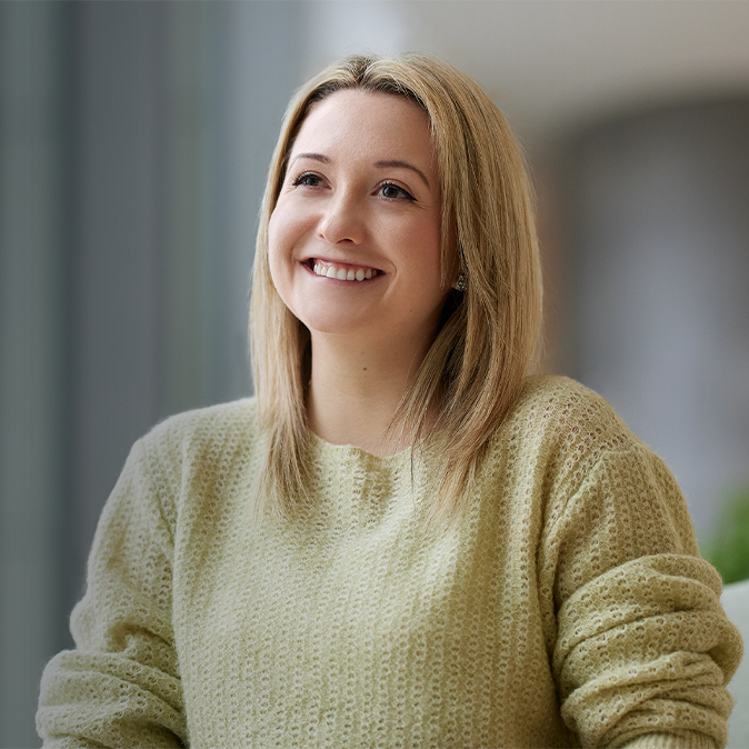 Georgia sourit, assise, le regard tourné vers la gauche.