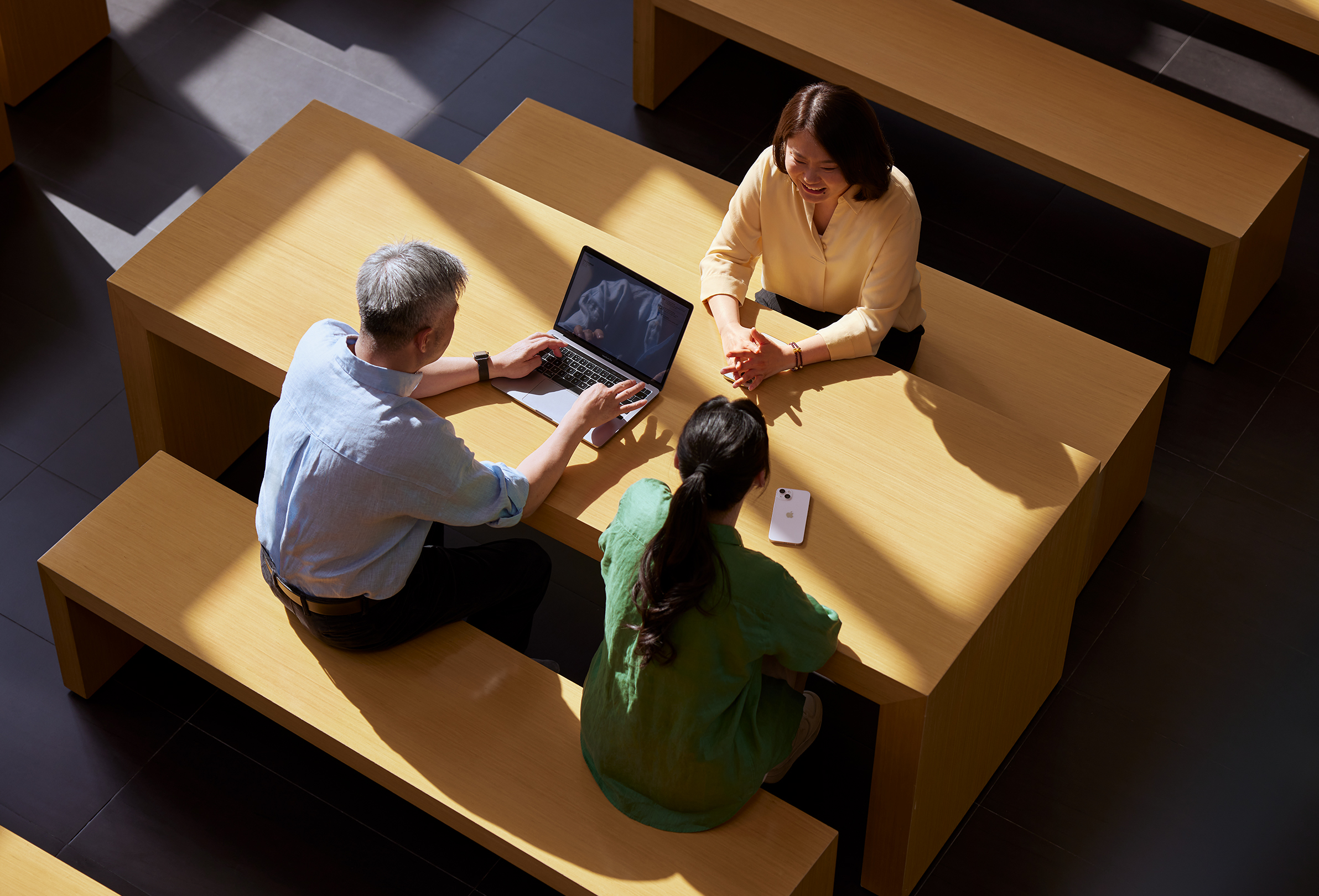 Trois membres du personnel d’Apple assis autour d’une table, l’un d’eux travaille sur un MacBook.