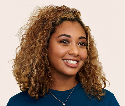 Persona del equipo de Apple Retail con el pelo largo y un collar sonriendo a la cámara.