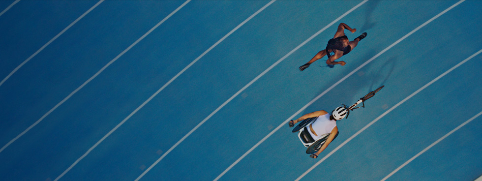 Two athletes racing each other on a track, one is running and the other is in a racing wheelchair.