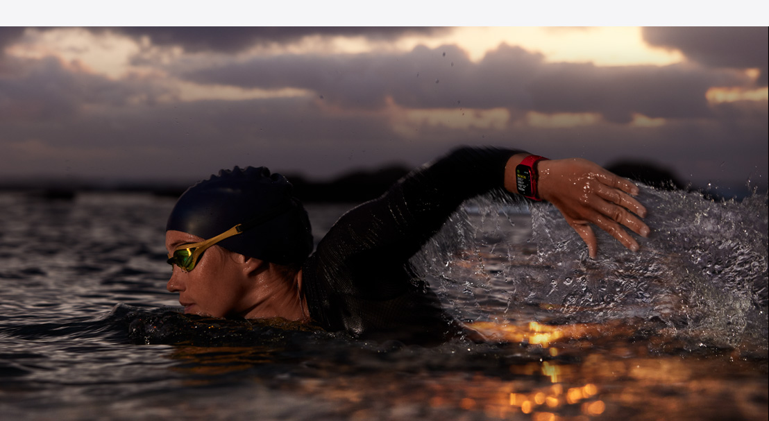 A man in a wetsuit wearing an Apple Watch Series 10 preparing to paddle out in the surf.