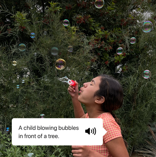 VoiceOver describing a photo and showing speech output. “A child blowing bubbles in front of a tree.”