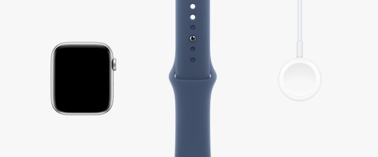 Stilt opp på rekke: maskinvaren i Apple Watch vist forfra, Sport Band i stjerneskinn og en magnetisk lader-til-USB‑C-kabel.