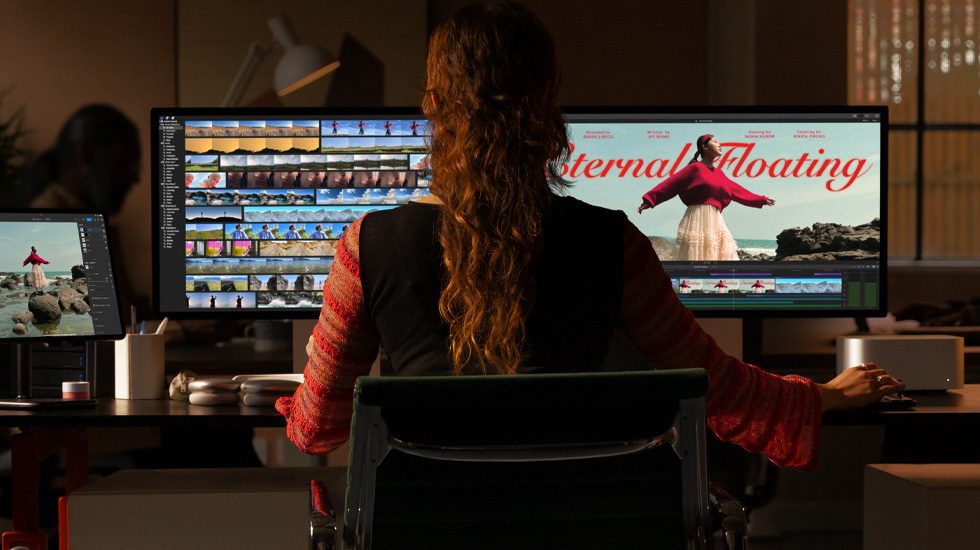 The back view of a person sitting in front of two monitors. The monitors show video content being edited.