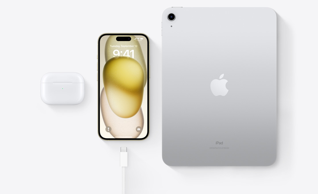 A birds-eye view of AirPods Pro, iPhone 15, and an iPad with a USB-C connector to demonstrate how all three devices can be charged using the same USB-C cable.