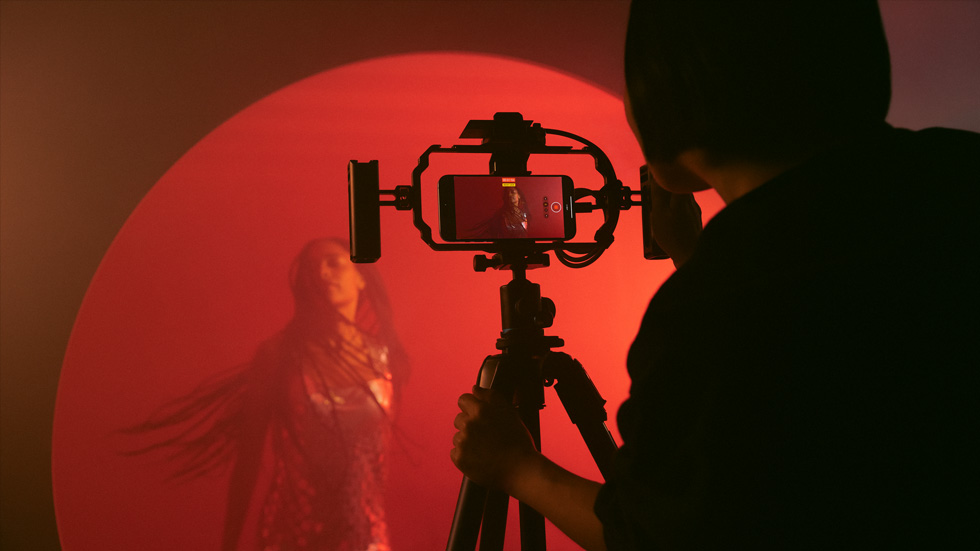 Et billede af en person, der bruger en iPhone på et stativ til at optage en farverig video af en kvinde