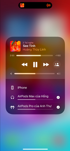 AirPods Pro trong hộp sạc bên cạnh iPhone, iPhone được kết nối với hai bộ AirPods, mỗi bộ có tùy chọn điều khiển âm lượng riêng.
