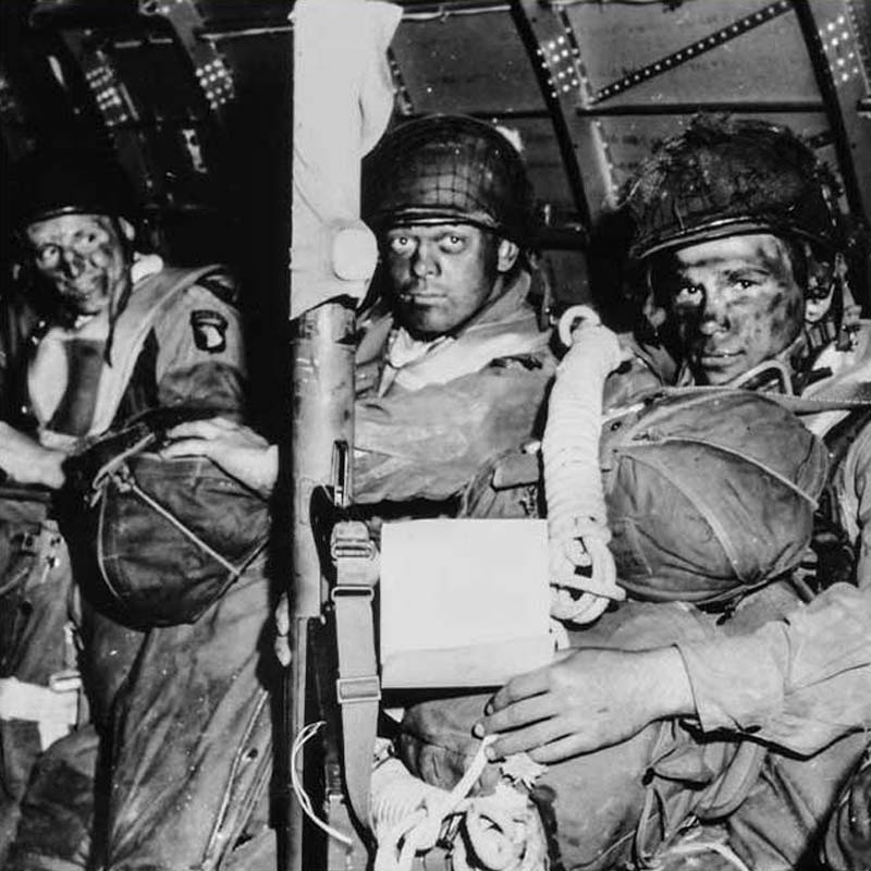 Resolute faces of paratroopers just before they took off for the initial assault of D-Day. Paratrooper in foreground has just read Gen. Eisenhower's message of good luck and clasps his bazooka in determination. Note Eisenhower's D-Day order in hands of paratrooper in foreground. Photo courtesy of National Archives and Records Administration.