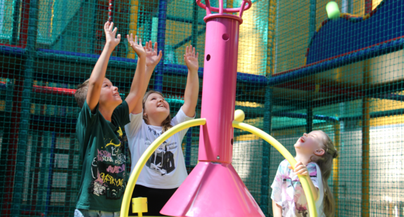 Drei Kinder stehen lachend um ein Spielgerät beim Klosterpark Adelberg.