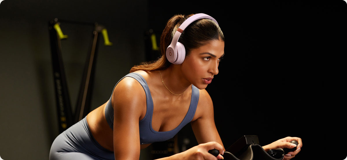 Woman on a stationary bike wearing Beats Solo 4 headphones