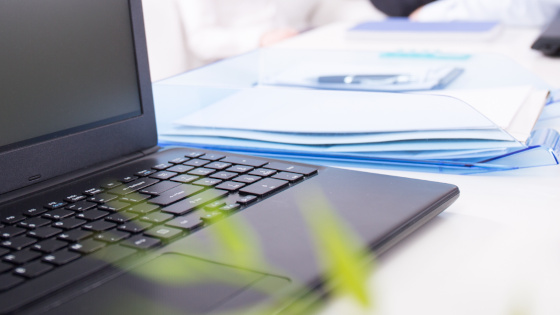 Laptop auf Schreibtisch, im Hintergrund Ablage mit Papier