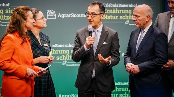 Gruppenbild: Bundesminister Özdemir spricht in der Halle des Erlebnisbauernhofs auf der Grünen Woche in ein Mikrofon.