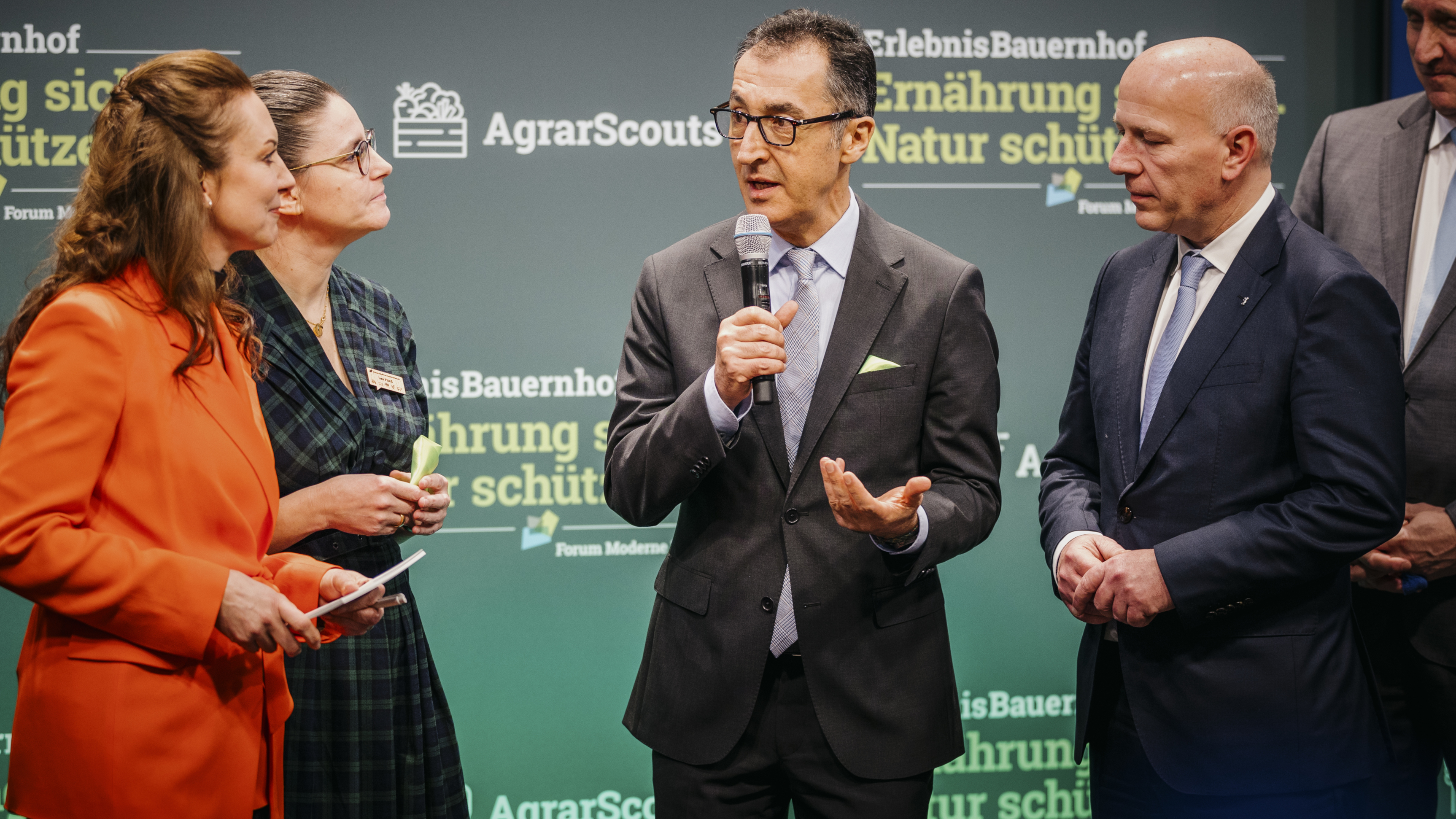 Gruppenbild: Bundesminister Özdemir spricht in der Halle des Erlebnisbauernhofs auf der Grünen Woche in ein Mikrofon.