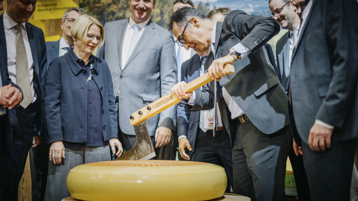 Bundesminister Özdemir schneidet mit einem Käsebeil in einen großen Käselaib.